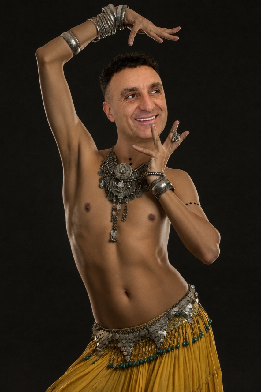 James Bulla, professional belly dancer, performing in dramatic stage costume against a near-black backdrop in Bolton
